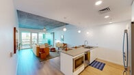 Located at 777 North Central Avenue in the heart of Phoenix, AZ, this two-bedroom, two-bathroom two-story residence blends modern urban design with warm, inviting interiors. The main floor is generously proportioned, anchored by an open-concept kitchen and living area that flows seamlessly together. The kitchen features a large island with a built-in sink, pendant globe lighting, white cabinetry, and a stylish tiled backsplash — equally suited for casual dining and entertaining. The adjacent living room is defined by exposed concrete ceilings, light hardwood flooring, and expansive floor-to-ceiling windows that flood the space with natural light and frame views of the Phoenix skyline. A distinctive concrete accent wall adds an industrial-chic character to the living area. The primary bedroom is a spacious retreat with wide-pane windows offering sweeping city views, an exposed concrete ceiling, and a ceiling fan. The second bedroom mirrors the clean, modern aesthetic. Both bathrooms are finished with terrazzo flooring, neutral cabinetry, oval mirrors, and pendant lighting. A standout feature is the large private outdoor terrace with bold green architectural framing, tiled flooring, and open city views — ideal for outdoor living in the Arizona sunshine.