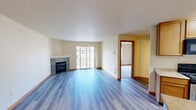 Located at 6801 S 133rd St in Seattle, WA, this one-bedroom, one-bathroom unit offers a practical and comfortable single-floor layout. The open living room is a standout, featuring light-toned hardwood-style flooring, warm neutral walls, and a tile-surround fireplace that serves as a focal point. Sliding glass doors lead to a private balcony, allowing natural light to fill the space and providing outdoor views of the surrounding neighborhood. The kitchen is efficiently designed with ample honey-toned cabinetry, light countertops, black appliances including a refrigerator, electric range, built-in microwave, and dishwasher, all complemented by matching hardwood-style flooring. A dedicated laundry room with a full-size washer and dryer adds everyday convenience. The bedroom offers plush carpeting, a large window with natural light, a baseboard heater, and a generously sized closet with built-in shelving and hanging rods. The bathroom includes a full tub-shower combo with tiled surround. Warm wood-toned baseboards and trim are consistent throughout, tying the unit together with a cohesive, clean aesthetic.