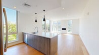 Located at 703 Whitney Ave in New Haven, CT, this contemporary 2-bedroom, 2-bathroom residence offers a thoughtfully designed single-level layout with clean lines and modern finishes throughout. The open-concept kitchen and living area serves as the heart of the home, anchored by a large center island with a white quartz countertop and wood-grain cabinetry, accented by striking black pendant lights. Stainless steel appliances, white upper cabinets, and a gas range complete the well-appointed kitchen. The living area is bathed in natural light from floor-to-ceiling windows and features a sleek built-in fireplace flanked by lush treetop views. Light hardwood flooring flows seamlessly throughout the entire residence, enhancing the bright, airy ambiance. The hallways connect two well-sized bedrooms, each offering clean white walls and generous closet storage — five closets in total are distributed across the unit. The two bathrooms are finished to a high standard, with the primary bath showcasing large-format marble-style tile, a glass-enclosed walk-in shower, a floating wood-tone vanity, and a full-width mirror. A dedicated laundry area adds everyday convenience, rounding out this polished and functional modern home.
