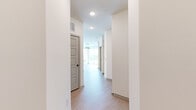 This well-appointed single-floor unit offers two bedrooms and two bathrooms across a thoughtfully designed layout. Light wood-tone flooring runs continuously throughout, lending warmth and visual cohesion to every room.

The combined kitchen and living area serves as the heart of the unit. The kitchen features two-tone cabinetry—white upper cabinets paired with soft blue-gray lowers—complemented by a white tile backsplash, stainless steel appliances, and a sleek island with an integrated sink. The living area extends naturally from the kitchen, with a sliding glass door that opens to a private balcony, offering outdoor views and ample natural light.

The bedrooms are bright and quietly styled, with large windows framing outdoor greenery. Each room connects to a dedicated closet; one features a walk-in design with built-in wire shelving for organized storage.

Both bathrooms are finished with clean, modern materials. The primary bathroom includes a wood-toned vanity with black hardware, a framed mirror, light tile flooring, and a glass-enclosed walk-in shower with white square tile surround.

The hallway connects all rooms efficiently, maintaining an open and airy feel throughout the unit.