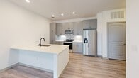 Located at 2311 Odell School Rd in Charlotte, NC, this well-designed one-bedroom, one-bathroom unit offers a clean, contemporary aesthetic throughout its efficiently laid-out single floor. Light wood-look flooring flows seamlessly across every room, complementing the crisp white walls and creating a bright, cohesive atmosphere.

The open-concept kitchen and living area serves as the heart of the unit. The kitchen is outfitted with sleek gray cabinetry, stainless steel appliances including a French door refrigerator, electric range, and over-the-range microwave, all accented by a white hexagonal tile backsplash. A kitchen island with an undermount sink and white countertops provides additional workspace and casual dining potential. Recessed lighting and ceiling fans enhance both functionality and comfort throughout the living areas.

The bedroom is a comfortable retreat, featuring dual windows with blinds that invite ample natural light and outdoor views. A dedicated closet provides practical storage. The bathroom continues the modern design language with gray cabinetry, a white countertop vanity, an LED-lit mirror, a wall-mounted storage cabinet, and light wood-look flooring that ties the space together. The overall ambiance is clean, modern, and move-in ready.
