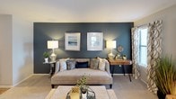 This well-appointed single-floor residence offers a thoughtfully designed layout that balances comfort and style. The living room serves as the heart of the home, showcasing a bold navy accent wall, plush carpeting, and multiple windows dressed with patterned curtains that invite generous natural light. A cozy seating arrangement and a direct-access door create an inviting and functional gathering space.

The galley-style kitchen features gray cabinetry, light quartz-style countertops, a classic subway tile backsplash, wood-look flooring, and black appliances including a range and refrigerator. A breakfast bar with bar seating connects the kitchen to the main living area, making it ideal for casual dining or entertaining.

The dedicated dining area is bathed in natural light from a bay of windows and comfortably accommodates a round table with upholstered seating, creating an intimate setting for meals.

The two bedrooms each offer carpeted floors, natural light from windows, and stylish accent walls. The primary bedroom includes a walk-in closet and direct access to the bathroom, providing a private retreat. The full bathroom features dark cabinetry, a light countertop vanity with a framed mirror, and a shower-tub combination with a decorative curtain and wood-look flooring.