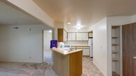 This single-floor unit offers a practical and well-organized layout designed for comfortable everyday living. The kitchen is a standout functional space, featuring white cabinetry with warm wood trim accents, ample upper and lower storage, a gas range, a refrigerator, and a built-in range hood. A peninsula-style breakfast bar connects the kitchen to the surrounding living area, creating an open flow between the spaces. The expansive open-concept living and dining area is finished with neutral-toned carpet and bright white walls, providing a clean and versatile backdrop. Natural light enters through multiple windows fitted with blinds, enhancing the overall sense of openness. The bedrooms are carpeted and generously sized, each with windows that allow natural light and outdoor views. One bedroom features a walk-in closet outfitted with built-in shelving, offering notable storage capacity. The bathroom includes a wide vanity with wood-trimmed cabinetry, an oversized mirror, and tile flooring that complements the rest of the unit. Throughout the space, the neutral color palette and consistent finishes create a cohesive and inviting atmosphere well-suited for a variety of living arrangements.