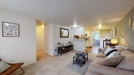 This single-story home efficiently arranges three bedrooms, one bathroom, a living room, and a combined kitchen-dining area within a thoughtfully organized floor plan. The carpeted living room serves as the central gathering space, featuring neutral walls, a wall-mounted mirror, and direct sightlines to both the hallway leading to the bedrooms and the kitchen beyond. Natural light enters through a sliding glass door that opens onto a private balcony, visually connecting the interior to the outdoors.

The kitchen features white cabinetry, hardwood flooring, black appliances including a range and refrigerator, and a pass-through counter that connects to the dining area. The dining space sits adjacent to the kitchen and benefits from additional natural light and balcony access via another sliding glass door. The primary bedroom accommodates a full-sized bed and includes a window. The two additional bedrooms are carpeted and feature sliding closet doors. The full bathroom includes a single-sink vanity with storage, a tub-shower combination, and hardwood flooring. A hallway connects the bedrooms and bathroom, completing the functional layout.