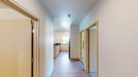 This well-designed single-floor residence offers a clean, contemporary aesthetic defined by light-toned wood trim, smooth white walls, and durable wood-look flooring throughout the main living areas. A central hallway connects the key spaces, providing an efficient and organized layout.

The kitchen is a standout feature, equipped with stainless steel appliances including a refrigerator, range, and microwave. Light wood cabinetry pairs with a dark, spacious countertop island that includes a sink, offering ample prep and storage space. A window above the counter brings in natural light.

The living area is generously sized and bathed in natural light, courtesy of multiple sliding glass doors that open to a shared balcony overlooking lush greenery. The open layout allows for flexible furniture arrangements and a seamless indoor-outdoor connection.

The bedrooms are carpeted for comfort and feature windows that provide natural light and exterior views. Each room offers a calm, neutral atmosphere suitable for rest or work.

A dedicated utility closet houses a stacked washer and dryer unit, while an adjacent closet with a hanging rod provides convenient storage. Light wood sliding doors maintain a cohesive design throughout. The space combines functional living with modern finishes in a thoughtfully arranged floor plan.