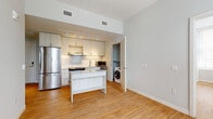 This single-floor residence features a thoughtfully designed layout spread across several rooms, as seen in the 3D floor plan. The open kitchen is outfitted with light wood cabinetry, subway tile backsplash, stainless steel appliances including a full-size refrigerator, electric range, and microwave. A white center island provides additional workspace, while a dedicated in-unit washer is conveniently positioned nearby. Track lighting illuminates the kitchen area, which connects to a generously sized living area featuring warm hardwood-style flooring throughout.

The bedrooms are bright and airy, benefiting from large windows fitted with horizontal blinds that frame urban cityscape views. The neutral gray walls and clean white trim create a crisp, modern aesthetic throughout.

The unit includes two bathrooms. The primary bathroom features large-format light tile flooring, an extended vanity with quartz countertops, gold-toned hardware accents, and multiple windows offering ample natural light. A second, fully accessible bathroom includes grab bars, an open-clearance vanity, and the same large-format tile, ensuring functionality and comfort. Throughout the unit, the clean, contemporary finishes and neutral palette contribute to a bright and cohesive living environment.