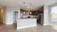 Located at 2155 Morris Basket Blvd in North Charleston, SC, this single-story unit offers a contemporary design with a neutral color palette and a practical, open layout. The kitchen serves as a central highlight, featuring dark espresso cabinetry extending to the upper walls, stainless steel appliances including a refrigerator, electric range, and microwave, and a large peninsula island with a light countertop and an integrated sink. Pendant lighting and track lighting illuminate the space, which flows seamlessly into an adjacent dining or living area with light wood-look flooring and a window providing natural light. A hallway connects the main living areas to the private rooms, with louvered closet doors adding a functional touch. The bedrooms feature plush carpeting, ceiling fans, and windows fitted with horizontal blinds that allow for natural light and outdoor views. Two full bathrooms are finished with wood-look flooring, dark vanity cabinetry, white countertops, large mirrors, and tub-shower combinations. The overall ambiance is clean, modern, and move-in ready, with consistent finishes carried throughout.
