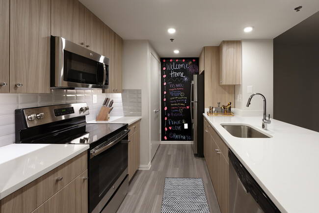 Renovated Package II kitchen with white quartz countertops, white tile backsplash, driftwood cabinetry, stainless steel appliances, and hard surface plank flooring - AVA Ballston Square