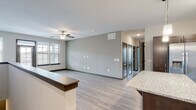 This two-story space offers a practical and modern layout with well-defined living areas across both levels. The kitchen serves as a central highlight, featuring rich dark-stained cabinetry, stainless steel appliances including a French door refrigerator, electric range, microwave, and dishwasher. A large granite-topped island anchors the space, complemented by pendant lighting, track lighting, a subway tile backsplash, and a built-in wine rack. Light wood-look flooring runs throughout the main living areas, creating a cohesive and clean aesthetic.

The open living area adjacent to the kitchen offers a ceiling fan, natural light from a window with blinds, and neutral gray walls that provide a versatile backdrop. Dark-paneled interior doors add a consistent design element throughout the space.

The bedrooms are carpeted and finished with ceiling fans, neutral gray walls, and dark baseboards, offering a comfortable and quiet atmosphere. The bathrooms feature light wood-look flooring, dark vanity cabinetry with granite countertops, and full tub-shower combinations with curved curtain rods and built-in shelving.

A dedicated laundry area accommodates full-size side-by-side washer and dryer units with overhead shelving. A carpeted staircase with a metal handrail connects the two floors, completing this functional multi-level layout.