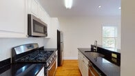 Located at 1 Langdon Square in Cambridge, MA, this single-floor residence offers a well-organized layout designed for functional living. Warm hardwood flooring flows consistently throughout the living areas and bedrooms, contributing to a cohesive and inviting ambiance. Crown molding adds a refined architectural detail throughout the space.

The kitchen is appointed with white cabinetry, dark granite countertops, and a full suite of stainless steel appliances, including a gas range, microwave, refrigerator, and dishwasher. A peninsula configuration opens the kitchen toward the main living area, which benefits from a large window overlooking lush greenery outside.

The bedrooms are generously proportioned, each featuring built-in closet systems with shelving and drawers for organized storage. Natural light fills these rooms through double windows, while baseboard heating ensures year-round comfort. A wall-mounted mini-split unit provides additional climate control in one bedroom.

Two bathrooms maintain a clean, classic aesthetic with white subway tile, black-and-white basketweave tile flooring, marble-topped vanities, and chrome fixtures. The overall design of this Cambridge residence balances timeless finishes with practical, modern amenities.