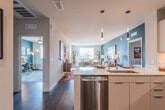 This thoughtfully designed single-floor residence showcases a seamless open-concept layout that connects the kitchen, dining, and living areas into one cohesive and functional space. The kitchen is outfitted with sleek white flat-panel cabinetry extending to the ceiling, a large quartz waterfall island with an undermount sink, stainless steel appliances including a refrigerator, range, and microwave, and a stylish tile backsplash. Pendant lighting illuminates the island, adding a refined touch to the space. The living area is anchored by a bold teal accent wall, large windows that invite abundant natural light, and direct views of the surrounding urban streetscape, creating a bright and welcoming atmosphere throughout. Dark hardwood-style flooring flows consistently across all areas, grounding the interior with warmth and continuity. The bedroom features a striking dark accent wall, direct access to a private outdoor balcony with urban views, and leads to a generously sized walk-in closet with dual hanging rails and built-in shelving. The bathroom is well-appointed with a modern vanity, large mirror, white quartz countertop, and a full soaking tub and shower combination. The private balcony offers a compact outdoor retreat with open city views, completing this well-rounded and contemporary residence.
