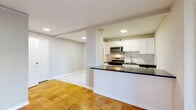Located at 8200 Wisconsin Avenue in the heart of Bethesda, MD, this 2-bedroom, 1-bathroom residence offers a thoughtfully designed single-floor layout. The open-concept living area is anchored by warm parquet wood flooring and large floor-to-ceiling sliding glass doors that lead to a private balcony, flooding the space with natural light and providing views of the surrounding cityscape.

The kitchen is outfitted with white shaker cabinetry, dark granite countertops, a marble-style tile floor, and a full suite of stainless steel appliances including a gas range, microwave, and refrigerator. A breakfast bar peninsula connects the kitchen to the living area, creating an easy flow for entertaining.

The spacious primary bedroom includes access to a well-organized walk-in closet with wire shelving systems, while the second bedroom features parquet flooring and a ceiling fan. Both rooms are served by a full bathroom with a granite-topped vanity, white cabinetry, tiled tub-shower combination, and neutral tile flooring. A connecting hallway with additional closet space completes the layout, offering practical storage throughout this well-appointed Bethesda residence.