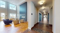 Located at 40 Bennett Rd in Englewood, NJ, this refined amenity floor showcases a thoughtfully designed collection of communal spaces that blend modern elegance with functional comfort. The grand lobby lounge immediately impresses with soaring double-height ceilings, a dramatic floor-to-ceiling slate fireplace adorned with gold-veined stone detailing, and rich herringbone hardwood flooring that flows throughout the entire level. A contemporary chandelier and abundant natural light from oversized windows further elevate the welcoming atmosphere. Adjacent to the lobby, a stylish lounge area features a sleek linear fireplace framed in stone, designer wingback chairs, and a plush area rug, creating an intimate setting for relaxation or socializing. A well-appointed kitchenette serves the common areas, complete with white quartz countertops, stainless steel beverage refrigerators, a wall-mounted television, and a striking herringbone-patterned tile accent wall. A separate dining and coworking area offers flexible seating arrangements, including banquette seating and dining tables, bathed in natural light from large windows. The fitness center is accessible via teal-framed glass doors directly from the lounge. French doors throughout provide seamless access to an outdoor terrace, connecting the interior spaces to the surrounding community.