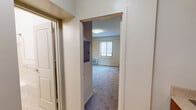This efficient single-floor unit offers a well-organized layout comprising one bedroom, one bathroom, and a connecting hallway. The entry hallway features tile flooring and provides direct access to the main living spaces, with an electrical panel conveniently recessed into the wall.

The bedroom is the largest room in the unit, finished with wall-to-wall carpet in a neutral tone that lends warmth underfoot. A set of mirrored sliding closet doors maximizes the sense of space while providing practical storage. Natural light enters through a window fitted with horizontal blinds, and a wall-mounted HVAC unit ensures year-round climate control. The walls are painted in a soft, muted yellow, creating a calm and understated atmosphere.

The bathroom is finished in a crisp, all-white palette with tile flooring in a marble-like pattern. It features a pedestal sink, a full-size bathtub with a tiled surround, and a curved shower curtain rod. Wall-mounted lighting above the mirror adds functionality to the clean, classic design.

A compact kitchen area visible in the floorplan overview includes cabinetry, a range, and a washer, making the unit fully self-contained. Overall, the space is practical and efficiently designed, offering essential amenities within a modest and manageable footprint.
