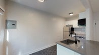 Located at 1036 Sanborn Ave in the vibrant Eastside neighborhood of Los Angeles, this thoughtfully updated single-floor unit blends modern finishes with a clean, cohesive design throughout. The open-concept layout connects the living area and kitchen seamlessly, with warm light wood flooring in the living space transitioning to bold dark hexagonal tile in the kitchen zone.

The kitchen is a standout feature, outfitted with crisp white cabinetry accented by matte black hardware, grey quartz countertops, and a striking geometric mosaic tile backsplash. Stainless steel appliances — including a gas range, over-the-range microwave, and refrigerator — complete the space with a functional, contemporary edge. A peninsula with an undermount sink and dark countertop serves as a natural divider between the kitchen and living room.

The living area is bright and airy, benefiting from multiple windows that invite natural light and views of surrounding greenery. A ceiling fan adds comfort and character overhead. A spacious walk-in closet provides generous storage with wrap-around shelving and rod systems.

The bathroom is elegantly finished with navy hexagonal floor tile, full white subway tile walls, a soaking tub with shower, grey-topped vanity, and matte black fixtures — creating a spa-like atmosphere with a modern monochromatic palette.