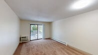 Located at 101 Longmeadow Dr in Holbrook, MA, this single-floor residence offers a practical and comfortable layout comprising one bedroom, one bathroom, a living room, kitchen, hallway, and three closets. The living room is a standout space, featuring wall-to-wall carpeting, a textured ceiling, and a large sliding glass door that opens to a private balcony, flooding the room with natural light and offering pleasant outdoor views of surrounding greenery. A wall-mounted HVAC unit and baseboard heating ensure year-round comfort. The spacious bedroom also features soft carpeting, a natural light-filled window with outdoor views, baseboard heating, and closet access, providing a calm and functional retreat. The kitchen is efficiently designed with cabinetry and countertop workspace, connecting seamlessly to the main living area via a pass-through or open counter. The full bathroom includes a tiled shower-tub combination with a curtain rod, toilet, and grab bar, finished in clean, neutral tones. Throughout the residence, neutral cream-colored walls, textured ceilings, and warm carpeted floors create a cohesive and understated aesthetic. Three closets offer generous storage solutions throughout the unit.