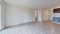This 600-square-foot, two-bedroom, one-bathroom apartment is located at 2627 N Market St, Unit 21, in Spokane, WA. The single-floor layout is designed for efficient use of space, connecting the kitchen and living area in an open-concept arrangement. The kitchen features dark wood cabinetry, a peninsula with a light countertop, a full-size refrigerator, electric range, dishwasher, and a stainless steel sink — all finished with light vinyl plank flooring that extends throughout the main living areas. The spacious living room benefits from a sliding glass door that opens to a private patio, allowing natural light to brighten the space. Baseboard heating is present throughout. A hallway connects the living area to the two carpeted bedrooms, each offering ample wall space. The primary bedroom measures 120 square feet and includes a wall-mounted AC unit, while the second bedroom features a sliding closet and baseboard heater. The full bathroom includes a soaking tub/shower combo, toilet, and matching light vinyl flooring. A textured ceiling is visible in the living area, adding subtle architectural character throughout this functional and well-laid-out Spokane apartment.