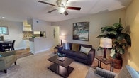 This single-story, one-bedroom, one-bathroom residence is thoughtfully designed to maximize functionality and comfort throughout its layout. The living room serves as the heart of the home, featuring warm neutral-toned walls, plush carpeting, a ceiling fan with integrated lighting, and a front-facing window that draws in natural light. The open sightline toward the kitchen creates a connected, airy feel throughout the common areas.

The galley-style kitchen is efficiently arranged with white cabinetry, a tile backsplash, wood-look flooring, and black appliances including a refrigerator, range, and dishwasher. A pass-through counter connects the kitchen to the living area, enhancing the open flow. Adjacent to the kitchen, a dedicated dining area accommodates a full dining set and features wood-look flooring and recessed lighting.

The bedroom is a calm retreat with soft carpeting, neutral walls, natural light from a window with blinds, and a walk-in closet for generous storage. The full bathroom includes a shower/tub combination, vanity with countertop storage, and wood-look flooring, completing this well-appointed residence.