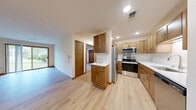 Located at 20950 George Hunt Cir in Waukesha, Wisconsin, this efficient and thoughtfully designed single-floor residence offers a comfortable layout across a combined living and functional space. The open living room is bright and welcoming, featuring light hardwood-style flooring and a large sliding glass door that floods the area with natural light while providing direct outdoor access to a green, landscaped view. The galley-style kitchen is well-equipped with warm wood cabinetry, white countertops, stainless steel appliances including a refrigerator, range, microwave, and dishwasher, complemented by recessed lighting and the same light flooring that carries throughout the main living areas. The bedroom offers a cozy retreat with plush carpeting, a ceiling fan, a dedicated closet, and a window overlooking the surrounding greenery. The full bathroom is clean and functional, featuring a wood-toned vanity with a white countertop, a large mirror, and a walk-in shower with built-in shelving. A connecting hallway ties all spaces together efficiently. Warm wood trim and neutral walls create a cohesive, inviting aesthetic throughout the entire residence.
