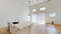 This three-floor space showcases a modern design aesthetic defined by clean lines, neutral tones, and high-quality finishes throughout. The open-concept kitchen serves as a central highlight, featuring a large island with marble-veined quartz countertops, an undermount sink, and white shaker cabinetry with matte black hardware. Stainless steel appliances, including a gas range with over-the-range microwave, complement a classic subway tile backsplash. The adjacent living area impresses with soaring double-height ceilings, clerestory windows that draw in abundant natural light, and large sliding glass doors providing outdoor access. Light-toned hardwood flooring flows throughout the main living areas, while plush carpeting adds comfort to the bedrooms. A metal railing staircase connects the floors, opening to an upper-level landing with wood flooring and additional living space. Bedrooms are bright and generously sized, each with windows fitted with blinds and ceiling fans. Bathrooms are finished with crisp white vanities, quartz countertops, and tile flooring; one features a walk-in shower with decorative herringbone tile. A dedicated laundry closet with full-size washer and dryer completes the practical amenities of this well-appointed space.
