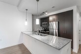 This single-floor residence offers a well-designed layout with a cohesive modern aesthetic. The open-concept living and kitchen area serves as the heart of the space, with light hardwood flooring that extends throughout the main living zone. The kitchen is outfitted with dark espresso cabinetry, granite countertops, a stainless steel undermount sink, and a full suite of stainless steel appliances including a refrigerator, range, and built-in microwave. A peninsula with a granite overhang provides additional workspace and casual seating potential, while pendant lighting and recessed track lighting illuminate the area effectively.

The bedrooms feature neutral carpet flooring and large windows fitted with blinds, offering views of the surrounding brick exterior architecture and allowing generous natural light. At least one bedroom includes a built-in closet with rod and shelf storage. The bathrooms present a clean, functional design: one includes a soaking tub with a tiled surround and chrome fixtures, while the other features a glass-door walk-in shower, wide-format tile flooring, and accessibility grab bars. Throughout the unit, the neutral color palette and consistent finishes create a bright, cohesive atmosphere.