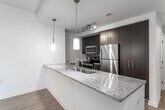 This single-floor residence offers a well-designed layout with a cohesive modern aesthetic. The open-concept living and kitchen area serves as the heart of the space, with light hardwood flooring that extends throughout the main living zone. The kitchen is outfitted with dark espresso cabinetry, granite countertops, a stainless steel undermount sink, and a full suite of stainless steel appliances including a refrigerator, range, and built-in microwave. A peninsula with a granite overhang provides additional workspace and casual seating potential, while pendant lighting and recessed track lighting illuminate the area effectively.

The bedrooms feature neutral carpet flooring and large windows fitted with blinds, offering views of the surrounding brick exterior architecture and allowing generous natural light. At least one bedroom includes a built-in closet with rod and shelf storage. The bathrooms present a clean, functional design: one includes a soaking tub with a tiled surround and chrome fixtures, while the other features a glass-door walk-in shower, wide-format tile flooring, and accessibility grab bars. Throughout the unit, the neutral color palette and consistent finishes create a bright, cohesive atmosphere.