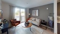 This single-floor residence offers a thoughtfully designed layout that balances modern aesthetics with everyday functionality. The open-concept kitchen is a standout feature, equipped with stainless steel appliances, rich dark wood cabinetry extending to the ceiling, light quartz countertops, and a spacious kitchen island with pendant lighting above — ideal for both meal preparation and casual dining. Light hardwood-style flooring runs throughout the main living areas, contributing to a clean, contemporary feel.

The living room is anchored by a bold charcoal accent wall and large sliding glass doors that open onto a private balcony, flooding the space with natural light and offering outdoor views. The area comfortably accommodates a full seating arrangement, making it well-suited for relaxing or entertaining.

The bedroom features plush carpeting, a ceiling fan with light fixture, and a large window dressed with blinds and curtains that allow for natural light control. A walk-in closet with wire shelving provides organized storage. The bathroom is finished with a wide vanity featuring a vessel-style sink, quartz countertop, dark wood cabinetry, and a glass-enclosed shower.

Completing the space is a dedicated laundry area with a stacked washer and dryer unit alongside additional shelving for storage.