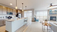 Located in Sun Prairie, Wisconsin, this single-floor residence offers a thoughtfully designed open-concept layout that seamlessly connects the kitchen, dining, and living areas. The kitchen is a functional centerpiece, featuring warm medium-toned cabinetry, light countertops, stainless steel appliances including a refrigerator, range, and microwave, a beverage cooler, and a spacious island with bar seating and pendant lighting overhead. Light hardwood-style flooring runs throughout the main living spaces, complementing the neutral color palette. The dining area sits adjacent to the kitchen, bathed in natural light from large sliding glass doors dressed with vertical blinds. The living room is bright and inviting, with oversized windows offering outdoor views and a striking corner stone fireplace that serves as a focal point. Carpeted bedrooms provide comfort and include closet storage, while the bathrooms are finished with taupe cabinetry, undermount sinks, large mirrors, and matte black fixtures. A well-proportioned hallway connects the private areas of the home to the main living spaces. Throughout, recessed lighting and clean architectural lines contribute to a modern yet welcoming ambiance.