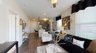 This single-floor residence offers a thoughtfully designed open-concept layout that seamlessly connects the living, dining, and kitchen areas. The living space is finished with rich hardwood-style flooring and features multiple windows dressed with black grommet curtains, allowing natural light to fill the room while maintaining a sleek, contemporary aesthetic.

The kitchen is a standout feature, showcasing grey shaker-style cabinetry, a classic white subway tile backsplash, and stainless steel appliances including a refrigerator, range, and built-in microwave. A granite-topped island with an undermount sink and seating for multiple guests serves as both a functional workspace and a social hub, illuminated overhead by a trio of stylish pendant lights.

The bedroom is a comfortable retreat with plush carpeted flooring, large windows offering natural light, and a ceiling fan. It connects directly to a generously sized walk-in closet with built-in shelving and hanging rods.

The ensuite bathroom is elegantly finished with hexagonal tile flooring, a dual-sink granite vanity with grey cabinetry, a large framed mirror, and a glass-enclosed shower. The cohesive design throughout—featuring granite countertops, grey cabinetry, and gold accents—gives the entire residence a polished, modern character.