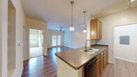 Located at 303 Wave Hill in Martinez, Georgia, this single-floor residence offers a thoughtfully designed open-concept layout that seamlessly connects the kitchen, dining, and living areas. The kitchen is equipped with warm honey-toned cabinetry, granite-style countertops, a peninsula with a double stainless steel sink, black appliances including a refrigerator and range, and pendant lighting that adds a polished touch. Track lighting further illuminates the space. Rich hardwood flooring extends throughout the main living areas, complementing the neutral, light-filled palette of the interiors. Crown molding and ceiling fans with light kits add refined detail to the living room, which is anchored by French doors that invite natural light and provide outdoor access. Built-in shelving along one wall offers practical display and storage options. The bedroom features plush carpeting, a ceiling fan, and a bright window with a view of the surrounding greenery. The bathroom includes a full soaking tub and shower combination with built-in shelving. A dedicated laundry area accommodates a full-size washer and dryer side by side, with additional storage shelving above. The overall ambiance is clean, comfortable, and move-in ready.