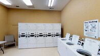 This single-floor laundry facility in Frisco is designed for practical, high-capacity use. The room features a clean, utilitarian layout with warm beige walls and light-colored flooring that give the space a bright, welcoming feel. Overhead fluorescent lighting ensures the area is well-lit throughout. A row of stacked commercial dryers lines the back wall, providing ample drying capacity, while a separate row of top-loading washers is positioned along the adjacent wall, offering convenient access. The machines are uniformly white, contributing to the room's organized and tidy appearance. HVAC vents are integrated into the ceiling, maintaining a comfortable environment. The straightforward design prioritizes functionality, making efficient use of the available space to accommodate multiple users simultaneously.