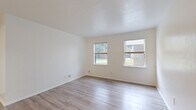 This single-story, 2-bedroom, 1-bathroom unit offers a practical and well-organized layout across a modest footprint. Light wood-style laminate flooring runs consistently throughout the home, complementing the crisp white walls and creating a clean, cohesive aesthetic.

The living room receives natural light through dual windows with views of surrounding greenery, providing a bright and airy atmosphere. The galley-style kitchen features white cabinetry, a built-in sink, light countertops, and a striking dark mosaic tile backsplash as a design accent, along with a full-size refrigerator and ample upper and lower cabinet storage.

The primary bedroom is a comfortable size, offering two windows that frame outdoor views and fill the room with natural light. The second bedroom also features a ceiling fan with light fixture and a window with outdoor views, promoting air circulation and brightness. Both bedrooms are equipped with closets, including a double-rod closet in one room for added storage.

The bathroom is finished in an all-white palette with tile surround, a combined tub and shower, and wood-style flooring. A dedicated utility room and hallway complete the floor plan. Throughout the home, the consistent flooring, neutral tones, and natural light create a simple and functional living environment.