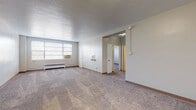 This single-floor, 1-bedroom, 1-bathroom unit offers a well-organized layout designed for comfortable everyday living. The expansive living room features wall-to-wall carpeting, neutral-toned walls, and a large window that invites natural light while housing a window AC unit and a baseboard radiator for year-round climate control. The open feel of the room is enhanced by its generous proportions, providing ample space for a variety of furniture arrangements.

The galley-style kitchen is efficiently designed with white cabinetry, dark granite-look countertops, a stainless steel refrigerator, a range, and a double sink — all set over rich hardwood-style flooring. Counter space lines both sides of the kitchen, offering practical storage and workspace.

The bedroom is a comfortable retreat, complete with wall-to-wall carpeting, a ceiling fan with light fixture, a window with blinds, a window AC unit, and a baseboard radiator. A closet provides convenient storage.

The bathroom features a classic black-and-white checkered tile floor, white square-tiled walls around the tub-shower combination, a dark-cabinetry vanity with a white basin sink, and a medicine cabinet mirror — lending the space a timeless, clean aesthetic throughout.