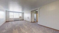 This single-floor, 1-bedroom, 1-bathroom unit offers a well-organized layout designed for comfortable everyday living. The expansive living room features wall-to-wall carpeting, neutral-toned walls, and a large window that invites natural light while housing a window AC unit and a baseboard radiator for year-round climate control. The open feel of the room is enhanced by its generous proportions, providing ample space for a variety of furniture arrangements.

The galley-style kitchen is efficiently designed with white cabinetry, dark granite-look countertops, a stainless steel refrigerator, a range, and a double sink — all set over rich hardwood-style flooring. Counter space lines both sides of the kitchen, offering practical storage and workspace.

The bedroom is a comfortable retreat, complete with wall-to-wall carpeting, a ceiling fan with light fixture, a window with blinds, a window AC unit, and a baseboard radiator. A closet provides convenient storage.

The bathroom features a classic black-and-white checkered tile floor, white square-tiled walls around the tub-shower combination, a dark-cabinetry vanity with a white basin sink, and a medicine cabinet mirror — lending the space a timeless, clean aesthetic throughout.