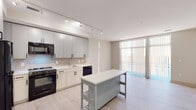 Located at 1400 Montana Ave NE in Washington, DC's vibrant Brookland neighborhood, this modern single-floor residence offers a thoughtfully designed open layout with clean finishes throughout. The kitchen is a standout feature, equipped with two-tone cabinetry in soft gray and light wood tones, a subway tile backsplash, white quartz countertops, and a full suite of black appliances including a gas range, dishwasher, refrigerator, and microwave. A central kitchen island provides additional prep and dining space, while track lighting overhead ensures excellent illumination. Light-toned hardwood-style flooring flows seamlessly throughout the unit, contributing to a bright and cohesive aesthetic. The living area benefits from floor-to-ceiling sliding glass doors fitted with vertical blinds, allowing abundant natural light and access to the outdoors. The bedroom is generously proportioned, featuring large windows with horizontal blinds that invite ample daylight while maintaining privacy. The bathroom is finished in a crisp, all-white palette with vertically stacked tile surrounding the soaking tub and shower, complemented by a gray vanity with white countertop and a large mirror. A walk-in closet is accessible directly from the bathroom, adding practical storage to this well-appointed residence.