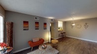 This premium two-bedroom, one-bathroom residence is thoughtfully designed across a single floor, offering a functional and well-connected layout. The living area serves as the centerpiece of the home, featuring dark hardwood-style flooring, neutral gray walls, a textured ceiling, and large windows fitted with vertical blinds that allow natural light to fill the space. A pendant light fixture adds a decorative touch near the dining area.

The kitchen is accessible via a pass-through counter with granite-style surfaces, white cabinetry, a double sink, and black appliances including a refrigerator and dishwasher. The pass-through design creates a seamless visual connection between the kitchen and main living space, and bar-height seating adds casual dining functionality.

Both bedrooms are carpeted for comfort. One bedroom features dual closets and a ceiling fan, providing ample storage and airflow. Windows in the bedrooms bring in natural light and outdoor views. A hallway connects the living areas to the bedrooms and the full bathroom, which includes a tub-shower combination with white tile surround. The overall ambiance is clean, modern, and move-in ready.