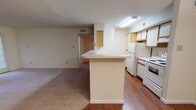 This single-floor residence offers a functional and straightforward layout. The living room serves as a central gathering space, highlighted by a classic brick fireplace flanked by two exterior doors with blinds, allowing for natural light while maintaining privacy. Soft carpet flooring extends throughout the living and bedroom areas, contributing to a warm, comfortable atmosphere.

The kitchen is efficiently designed with light wood cabinetry, white appliances including a range, dishwasher, and refrigerator, and a peninsula that provides both additional counter space and a natural division between the kitchen and adjacent dining or living areas. Hardwood flooring runs through the kitchen and entry zones, offering easy maintenance and visual contrast to the carpeted rooms.

The bedroom is a well-proportioned space featuring a ceiling fan with integrated lighting, a window with blinds that introduces natural light, and plush carpet underfoot. An additional room with hardwood flooring and a dedicated entry door provides flexibility as a bedroom or office.

The bathroom is clean and simply appointed, featuring a tiled tub-shower combination, a toilet, and tile flooring. Throughout the residence, neutral wall tones and standard ceiling heights create a bright, cohesive environment well-suited for everyday living.