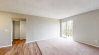 This 1-bedroom, 1-bathroom unit is thoughtfully laid out across a single floor, making efficient use of its space. The open living room features soft carpeting, neutral walls, and a textured ceiling, with a sliding glass door that opens to a private balcony overlooking mature trees — bringing in natural light and outdoor views. The transition from the living area into the kitchen is marked by a shift to warm hardwood-style flooring, which continues throughout the kitchen and hallway. The galley-style kitchen is outfitted with white cabinetry, granite-look countertops, a stainless steel sink, and black appliances including a full-size refrigerator and range, providing ample storage and prep space. Adjacent to the kitchen, a dedicated dining area offers room for a table and benefits from the same hardwood-style flooring and a thermostat panel on the wall. The bedroom is a generously sized, carpeted retreat with a natural window and an open closet with a built-in hanging rod for convenient storage. The bathroom features a full-size tub and shower combo with clean white surround, chrome fixtures, and hardwood-style flooring. A hallway connects all rooms efficiently, completing this practical and comfortable layout.
