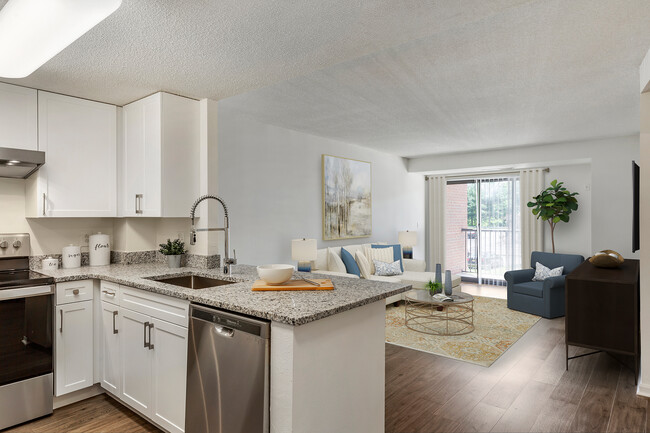 Renovated Package III kitchen and living area with white cabinetry, grey granite countertops, stainless steel appliances, and hard surface flooring - eaves Washingtonian Center