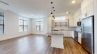 Located at Colony Plaza in Charlotte's SouthPark area, this single-floor residence offers a thoughtfully designed open-concept layout with contemporary finishes throughout. The expansive living area is anchored by rich hardwood flooring and bathed in natural light from multiple large windows with modern blinds, creating a bright and welcoming atmosphere. A ceiling fan adds comfort to the generous living space.

The kitchen is a standout feature, showcasing a large granite-topped island with pendant lighting overhead, crisp white shaker cabinetry, open shelving with wine storage, a herringbone tile backsplash, and a full suite of stainless steel appliances including a refrigerator, range, and built-in microwave. The seamless flow between the kitchen and living area makes the space ideal for both everyday living and entertaining.

The bedrooms are carpeted for comfort and receive ample natural light through well-positioned windows. Each bathroom is finished with granite vanity countertops and large-format light tile flooring. One bathroom features a soaking tub with classic white subway tile surround, while both bathrooms provide convenient access to walk-in closets with built-in shelving, offering excellent storage solutions throughout.