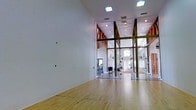 This single-floor athletic facility is thoughtfully designed for both competitive play and comprehensive fitness training. At its core is a full-sized indoor court with pristine hardwood flooring and dramatically high ceilings that allow for uninhibited play. The court is enclosed by floor-to-ceiling glass walls, offering clear sightlines into the adjacent fitness area and allowing natural light to flow freely throughout the space.

Exposed wooden trusses and beams add architectural character to the soaring overhead structure, blending a rustic aesthetic with a clean, modern interior finished in crisp white. Recessed ceiling lighting ensures consistent, bright illumination across both the court and surrounding areas.

The connected fitness area is well-equipped with exercise machines and training equipment, making this facility suitable for a full workout regimen beyond court sports. Large windows in the gym area invite natural light and offer views of the surrounding landscape, enhancing the overall sense of openness.

The seamless integration of the court and gym areas, combined with the generous vertical space, exposed timber accents, and glass partitions, creates an athletic environment that is both functional and visually impressive — ideal for serious training and recreational play alike.