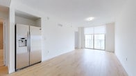 This single-floor unit offers a clean, contemporary design characterized by crisp white walls, light wood-tone flooring, and an open-concept layout that connects the main living areas seamlessly. The kitchen is well-appointed with flat-panel wood-grain cabinetry, granite countertops, and a full suite of stainless steel appliances, including a side-by-side refrigerator with ice maker, electric range, built-in microwave, and dishwasher. The kitchen opens directly into a generously sized living area that benefits from an abundance of natural light.

Floor-to-ceiling sliding glass doors lead to a balcony, framing expansive views of the surrounding cityscape and what appears to be a waterfront beyond—a notable highlight of the space. The bedrooms are well-sized, each featuring light wood flooring, large windows with roller shades offering city views, and easy access to the bathroom areas. The bathroom is finished with a wood-grain vanity, granite countertop, undermount sink, chrome hardware, and a large mirror. Throughout the unit, the consistent use of neutral tones and modern finishes creates a cohesive, bright, and functional living environment.