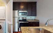 Located at 650 Route 23 in Wayne, NJ, this single-floor residence offers a thoughtfully designed layout with quality finishes throughout. The kitchen is a standout feature, showcasing rich dark-espresso cabinetry, granite countertops, and a full suite of stainless steel appliances including a refrigerator, range, and built-in microwave. A dedicated laundry closet conveniently houses a stacked washer and dryer unit just steps from the kitchen. Rich hardwood-style flooring extends through the main living areas, adding warmth and visual continuity. The spacious living room is bathed in natural light from a large window fitted with blinds and features built-in shelving — a functional and decorative focal point ideal for storage or display. The bedrooms are carpeted for comfort and each benefits from windows that frame views of surrounding greenery. Two well-appointed bathrooms mirror the kitchen's aesthetic with matching dark cabinetry, granite vanity tops, framed mirrors, and tub-shower combinations with clean white tile surrounds and hardwood-style flooring. The overall ambiance is clean, modern, and move-in ready, combining practical amenities with refined finishes in a convenient Wayne, NJ location.