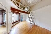 Located at 2205 2nd Ave in Seattle's vibrant Belltown neighborhood, this loft-style unit offers a distinctive blend of historic character and urban living. The living room serves as the heart of the space, showcasing soaring ceilings with exposed wood beams and painted wood-plank ceiling panels that lend an industrial-meets-rustic charm. A striking exposed brick column and surround frames a large picture window, flooding the room with natural light and offering views of the surrounding cityscape. Warm hardwood floors run throughout the main level, adding to the inviting atmosphere. A loft level, accessible via a metal-and-wood ladder staircase, provides additional functional space overhead. The compact kitchen features wood-toned butcher block countertops, white cabinetry, a stainless steel sink, and essential appliances including a stove and refrigerator. The bathroom includes a tiled tub-shower combination. An entrance corridor leads into the unit, with two closets offering practical storage solutions. Baseboard heating ensures year-round comfort. This uniquely characterful space reflects the architectural heritage of the building while offering the essentials for efficient urban living in one of Seattle's most walkable and dynamic neighborhoods.