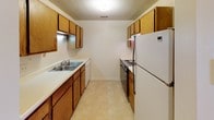 This single-floor unit offers a well-organized layout designed to maximize functionality. The living room serves as the central gathering space, featuring plush carpeting, a ceiling fan with integrated lighting, and a sliding glass door framed by vertical blinds that allows natural light to fill the room. The entry door opens directly into this area, creating a welcoming flow throughout the unit.

The galley-style kitchen is efficiently arranged with warm wood-toned cabinetry lining both sides, providing ample upper and lower storage. Light countertops offer workspace alongside a double-basin sink, dishwasher, electric range, and refrigerator. Light tile flooring completes the practical aesthetic of the space.

The bedroom is a comfortable, carpeted room featuring a ceiling fan with lighting and a sliding glass door with vertical blinds offering additional natural light. The room connects to generous closet storage, including a standard clothes closet and a shelved linen or utility closet accessible via bifold doors. An additional carpeted room with a window provides flexible use as a study or secondary space.

The full bathroom includes a single-sink vanity with wood cabinetry, a large mirror, a toilet, and a tub/shower combination. Textured ceilings are consistent throughout the unit.