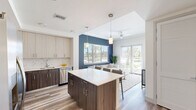 Located at 401 SE Central Pkwy in Stuart, Florida, this single-floor unit offers three bedrooms and one bathroom within a thoughtfully designed, efficiently arranged floor plan. The open-concept layout connects the kitchen and living room, creating a cohesive, airy feel that maximizes the available space.

The kitchen is a standout feature, showcasing a two-tone design with light upper cabinetry and dark wood-grain lower cabinets, paired with white quartz countertops and a marble-look tile backsplash. A central island with seating provides additional workspace and casual dining options. Stainless steel appliances, including a French door refrigerator, range, microwave, and dishwasher, complete the modern aesthetic.

The living room flows naturally from the kitchen and is anchored by a bold navy accent wall, large windows, and glass patio doors that invite abundant natural light and outdoor views of palm-lined surroundings. Wood-look plank flooring extends throughout the unit, lending warmth and continuity.

The primary bedroom is generously sized and includes a walk-in closet with built-in shelving. The bathroom features a long vanity with quartz countertops, wood-toned cabinetry, a frameless glass walk-in shower, and light tile flooring, delivering a clean, contemporary finish.