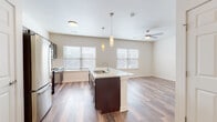 This single-floor residence offers a thoughtfully designed open-concept layout that seamlessly connects the kitchen and living areas, creating a bright and airy atmosphere. The kitchen serves as the centerpiece of the space, anchored by a large island with a crisp white countertop, an integrated sink, and elegant pendant lighting overhead. Dark espresso cabinetry provides rich contrast against the light surfaces, while stainless steel appliances — including a refrigerator, range, and over-the-range microwave — add a polished, contemporary touch. Multiple windows dressed with white blinds allow natural light to fill the space throughout the day. The open living area extends naturally from the kitchen and is complemented by a ceiling fan, adding both comfort and functionality. Consistent hardwood-style flooring runs throughout the main living spaces, lending warmth and visual continuity. A dedicated bedroom area offers a quiet retreat, with easy access to a well-sized bathroom featuring dark vanity cabinetry, a white countertop, a bathtub with towel bars, and matching hardwood-style flooring. The overall design aesthetic is clean, modern, and neutral, making this a highly versatile and move-in-ready space.