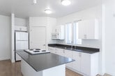 Located at 540 E 500 S in Salt Lake City, Utah, this one-bedroom, one-bathroom residence offers a well-designed single-floor layout with a clean, modern aesthetic. The interior is defined by crisp white walls, light wood-style flooring in the main living areas, and an abundance of natural light streaming through large windows fitted with blinds.

The living area is bright and open, featuring tall windows that frame outdoor views of the surrounding neighborhood, complemented by a ceiling fan overhead. The space flows seamlessly into the kitchen, which is equipped with white cabinetry, dark countertops, a double-basin sink, a cooktop island, a refrigerator, a range, a microwave, and ample upper and lower cabinet storage.

The bedroom is a comfortable, carpeted retreat with windows providing natural light and a tray ceiling detail that adds architectural interest. A dedicated closet offers convenient storage. An in-unit stacked washer and dryer is also present, adding everyday practicality.

The bathroom features warm tile flooring, a white vanity with dark countertop, a full tub-shower combination, and clean, neutral finishes throughout. A hallway with light wood-style flooring connects the rooms, maintaining the home's cohesive and tidy design. Overall, the unit offers a functional, well-lit living environment in a central Salt Lake City location.