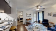 Located at 108 Valrico Station Rd in Valrico, FL, this well-designed one-bedroom, one-bathroom residence makes smart use of its compact footprint. The open-concept living and kitchen area serves as the heart of the home, featuring rich hardwood-style flooring, a ceiling fan with light fixture, and windows dressed with blinds and navy curtains that invite natural light while maintaining privacy. The kitchen is appointed with dark cabinetry, granite-style countertops, a breakfast bar with seating for two, stainless steel refrigerator, and black appliances including a gas range and built-in microwave. The living area offers a comfortable, airy atmosphere with room for a full seating arrangement. The bedroom is carpeted for warmth and comfort, featuring its own ceiling fan, a window with natural light, and ample closet access — with three closets total throughout the unit providing generous storage. The full bathroom includes a tub/shower combination with crisp white tile surround. Additional highlights include an in-unit laundry area and a private patio, ideal for outdoor relaxation. The textured ceilings and neutral wall tones throughout lend a clean, cohesive aesthetic to the entire space.
