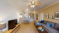 Located at 25800 SW Canyon Creek Rd in Wilsonville, Oregon, this well-appointed 2-bedroom, 3-bathroom single-floor residence offers a thoughtfully designed open-concept layout with light wood-tone flooring throughout the main living areas. The combined living and dining area is anchored by a corner gas fireplace and ceiling fan, with large windows framing views of the surrounding natural landscape and filling the space with abundant natural light. A picture rail along one wall adds a curated, gallery-like touch to the living room. The kitchen features a peninsula with a white quartz countertop, stainless steel appliances including a refrigerator and microwave, light wood cabinetry, track lighting, and a stainless steel sink — all open to the dining and living areas for seamless entertaining. Built-in shelving provides additional storage and display space. The primary bedroom is a comfortable retreat with sliding glass door access to a private balcony overlooking greenery, plush carpeting, and a ceiling fan. The second bedroom features large windows with outdoor views and soft carpeting. The bathrooms are clean and bright, with light wood vanities, white countertops, and a tub-shower combination. Two closets and thoughtfully placed storage throughout complete this functional and inviting home.